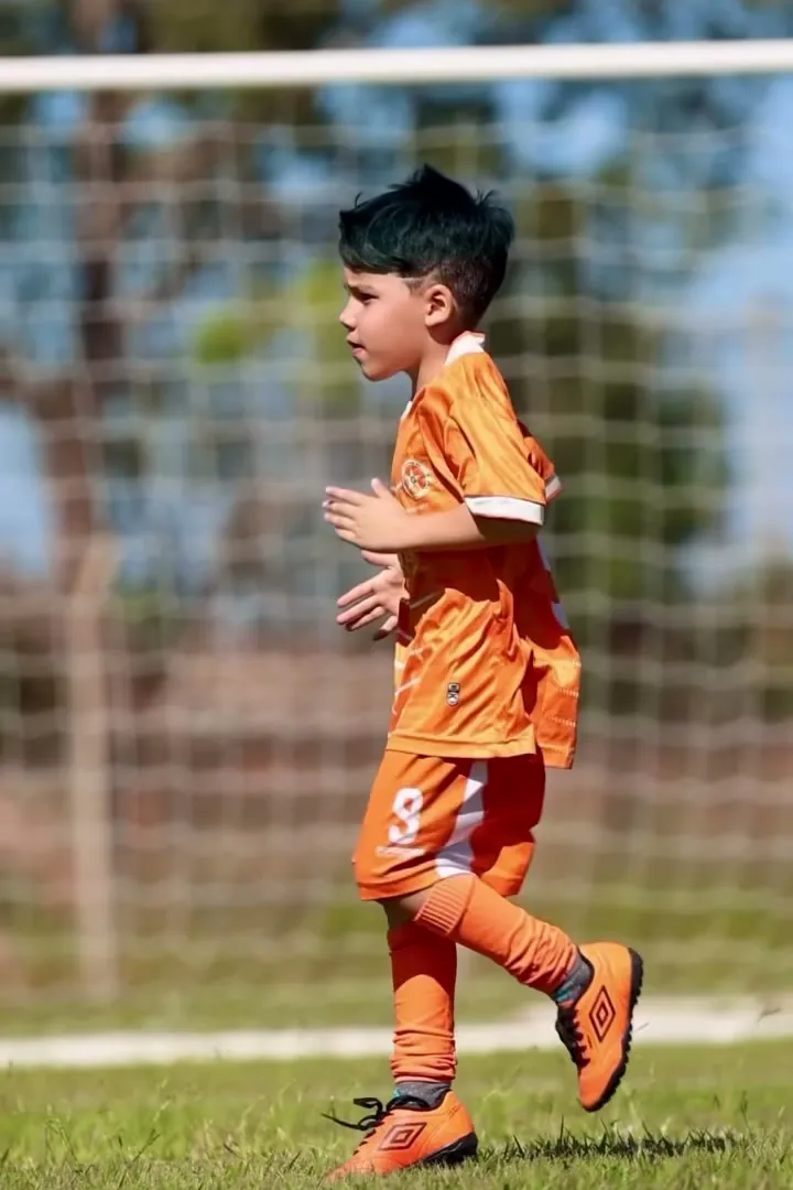 Aluno de uniforme laranja caminhando em campo